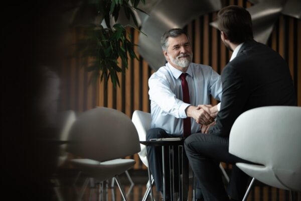 Business partnership meeting in office. Mature businessman shake hands with a younger colleague